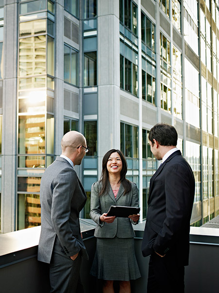 A female professional and two male professionals are engaging in trivial conversation on the balcony of the building.