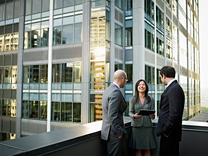 A female professional and two male professionals are engaging in trivial conversation on the balcony of the building.