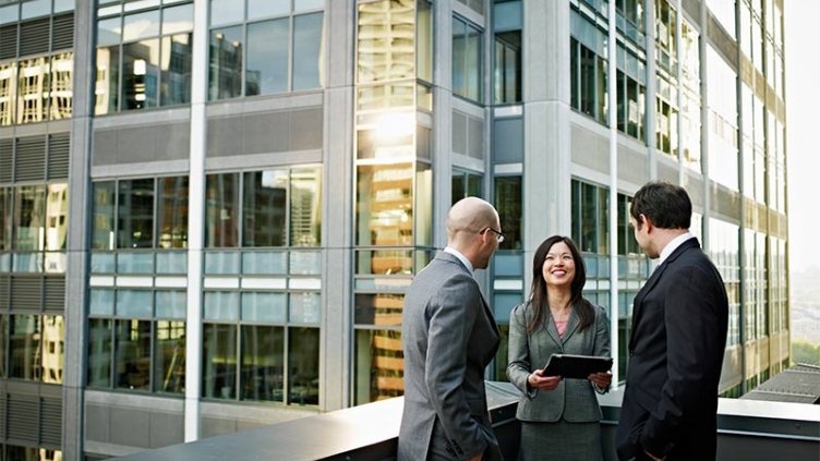 A female professional and two male professionals are engaging in trivial conversation on the balcony of the building.