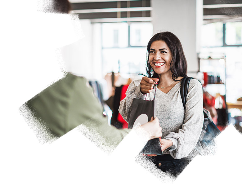 A clothing store clerk handing a smiling customer her purchased items in a paper bag.