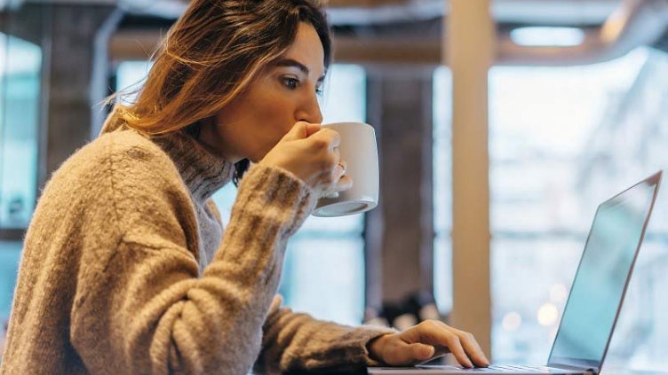 A woman having a cup of coffee while working on her laptop inside the office