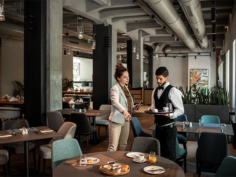 Hotel manager providing guidance to waiter in the restaurant.